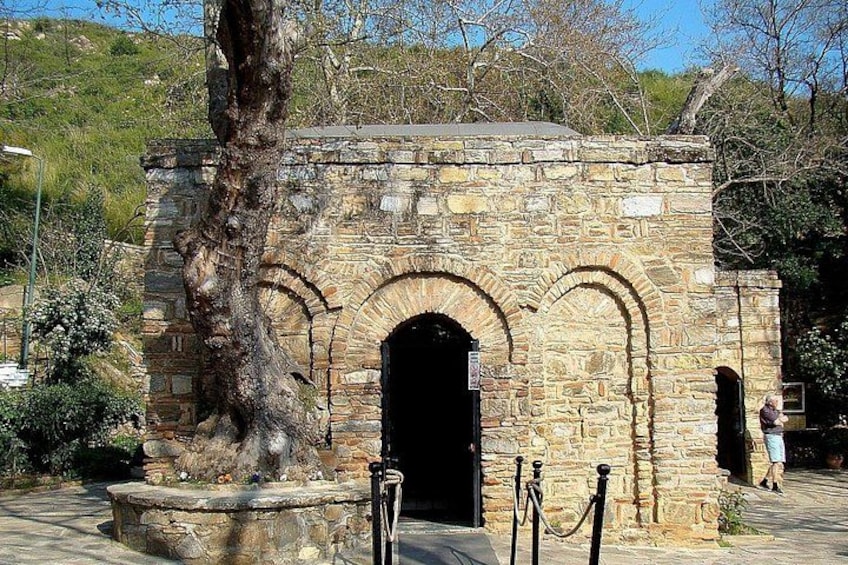 Un bâtiment en pierre doté d’une entrée en arc de cercle, entouré d’arbres et bordé d’une zone pavée. 2