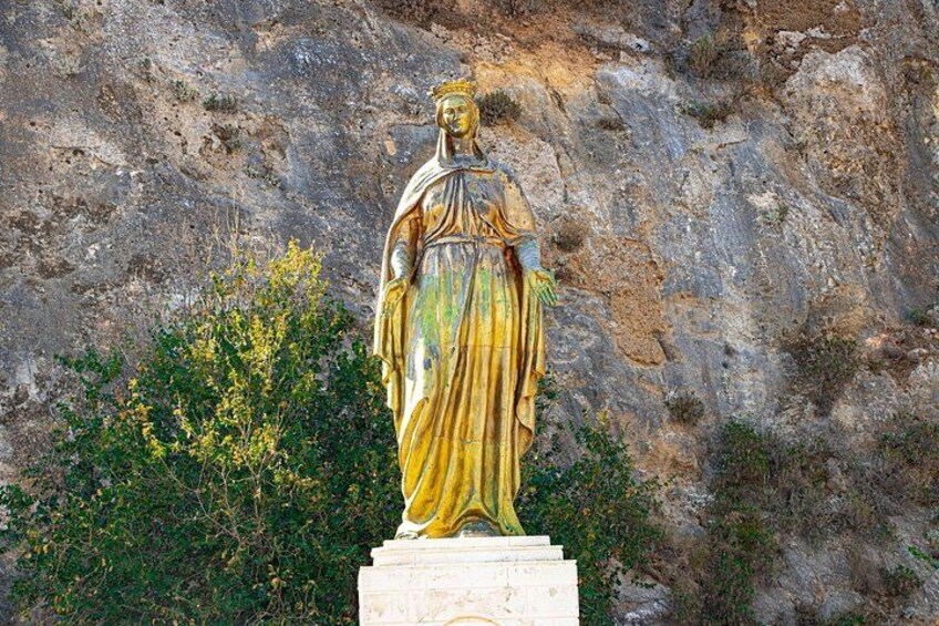 Una estatua dorada de una figura vestida sobre un pedestal, frente a un risco con vegetación escasa. 3