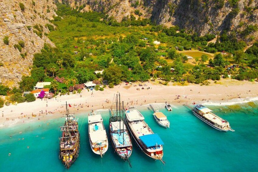 Zona costera con barcos amarrados en un muelle, una playa de arena y abundante vegetación al fondo. 5
