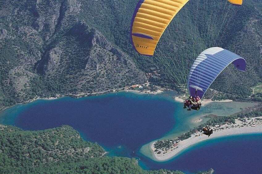 Un parapentista volando sobre una zona costera con un lago y colinas boscosas. 1