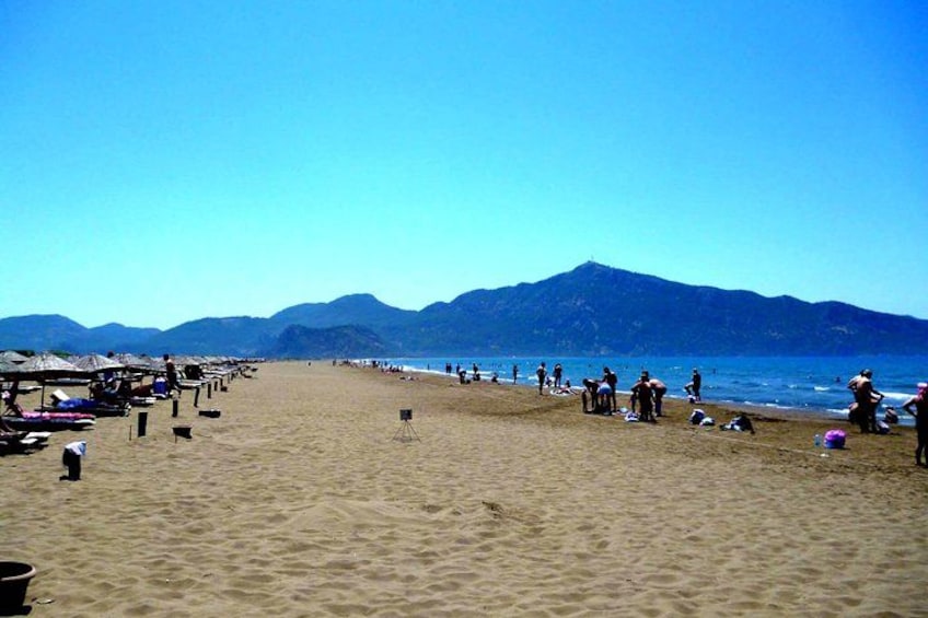 A beach with people, umbrellas, and mountains in the background. 3