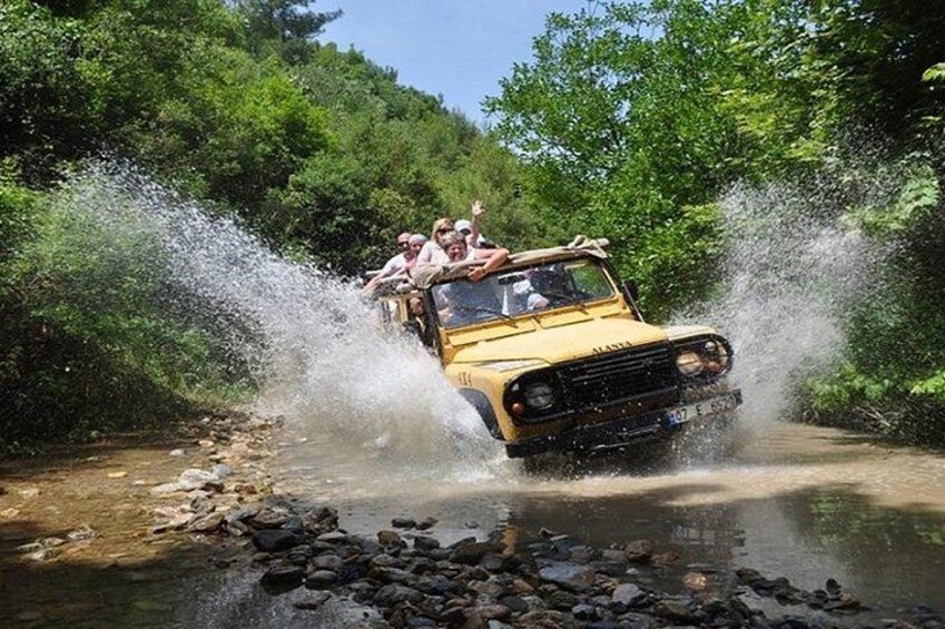 A yellow vehicle driving through a shallow water crossing surrounded by lush greenery. 1