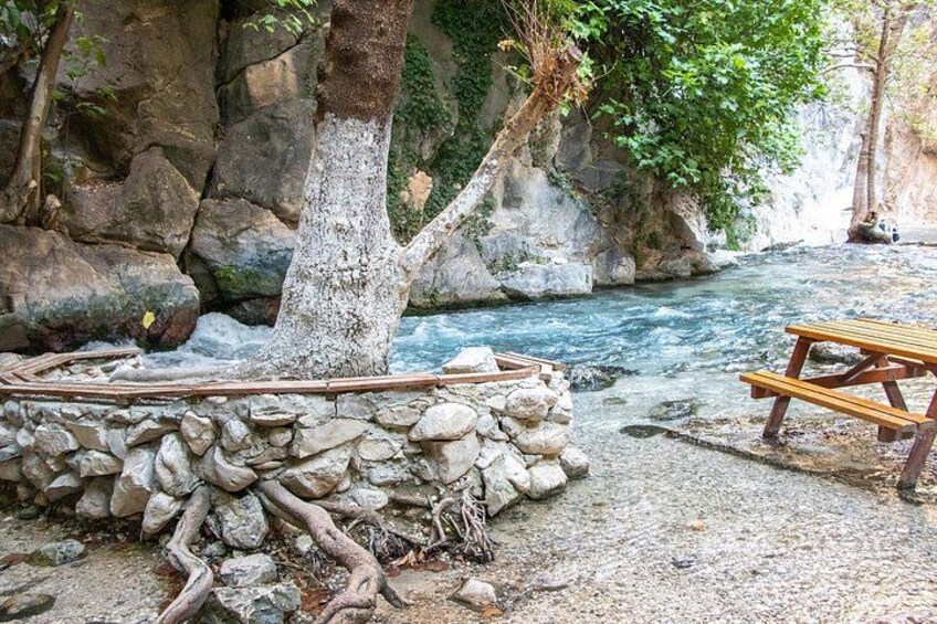 A rocky riverbank with a wooden bench and a stone wall. 2