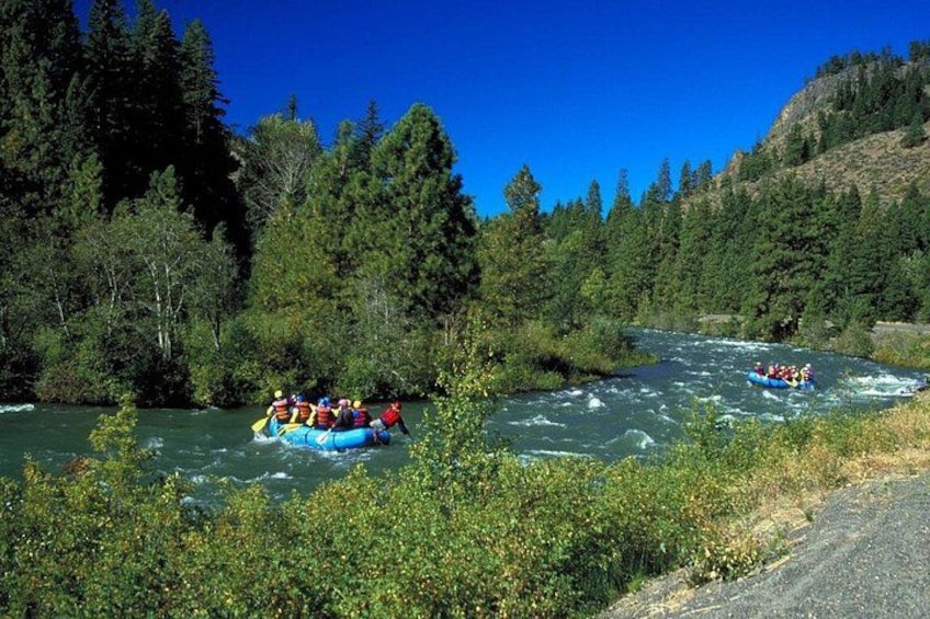 Un río con un grupo de personas haciendo rafting en botes inflables azules. 3