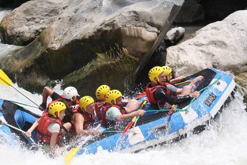 Un grupo de personas en una balsa azul navegando por un río con rápidos, rodeado de rocas y grandes rocas. 2