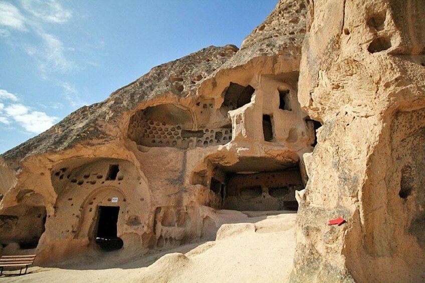 Una cueva excavada en roca con múltiples entradas y un banco. 2
