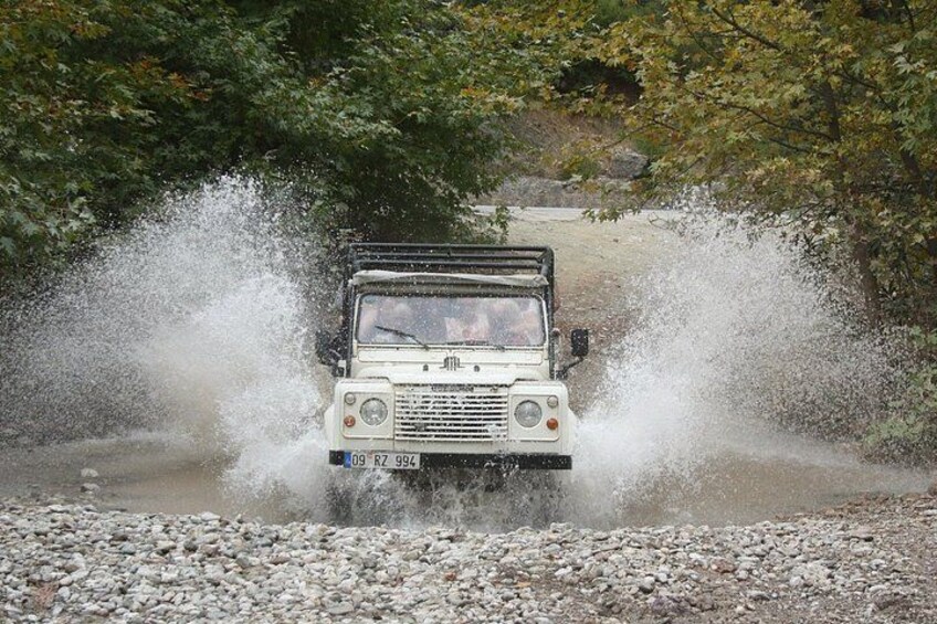 A white off-road vehicle driving through a shallow water crossing, splashing water around. 2