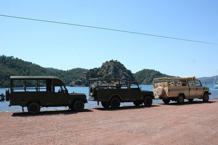 Three military jeeps parked on a dirt area by a lake with a mountainous backdrop. 5