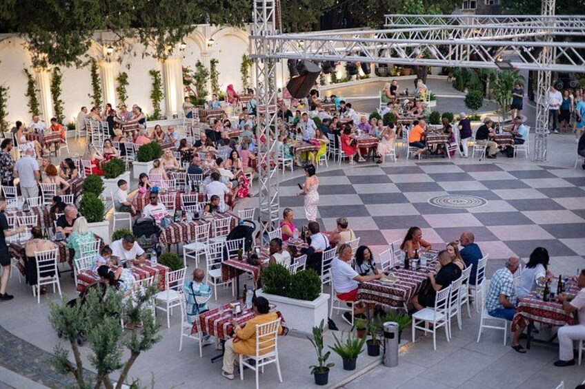 An outdoor café with tables and chairs, surrounded by trees and a checkered floor. 3