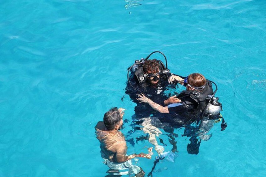 Two people in a swimming pool, one assisting the other with a diving apparatus. 4