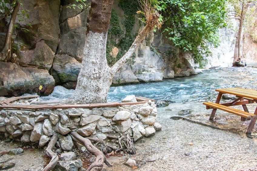 A rocky riverbank with a wooden picnic table and a tree. 2