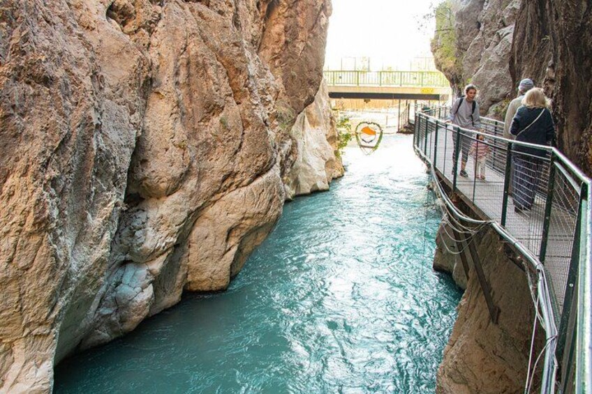A rocky canyon with a river, a pedestrian bridge, and a person walking. 3