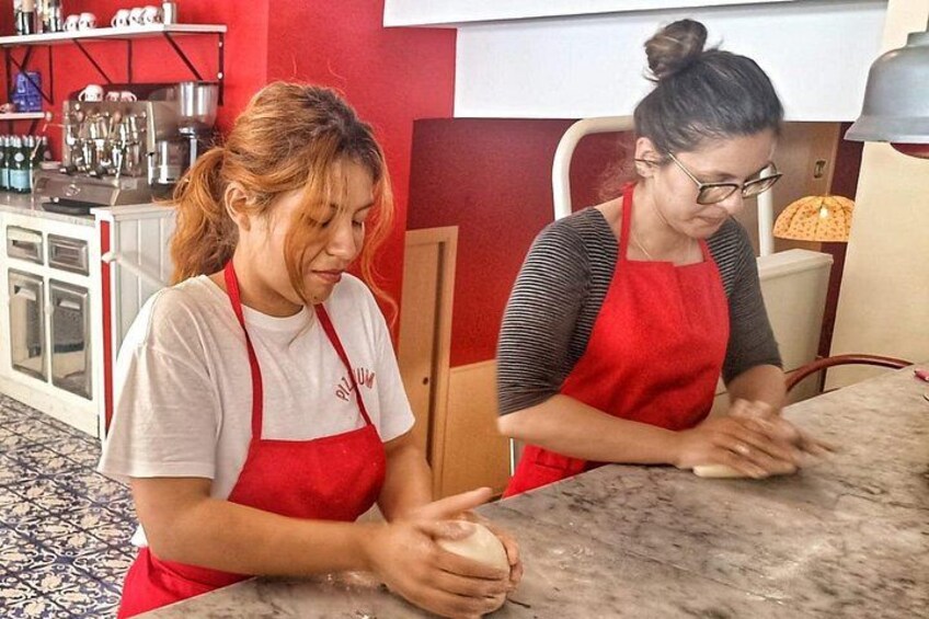 Two individuals wearing red aprons, one in a white shirt and the other in a striped shirt, working at a marble counter in a kitchen setting. 5