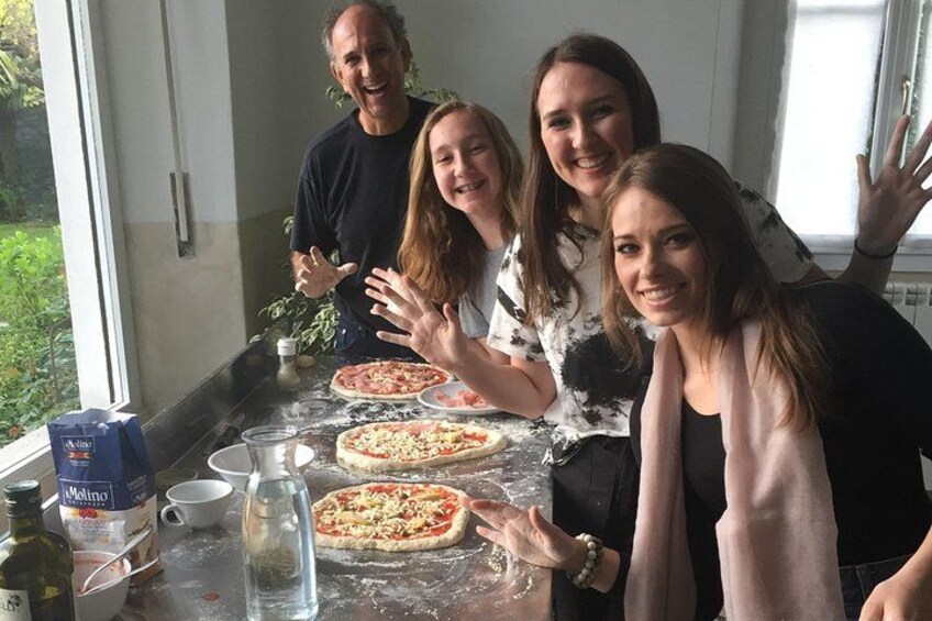 Four people around a table with pizza dough and ingredients, a window, and a plant. 1