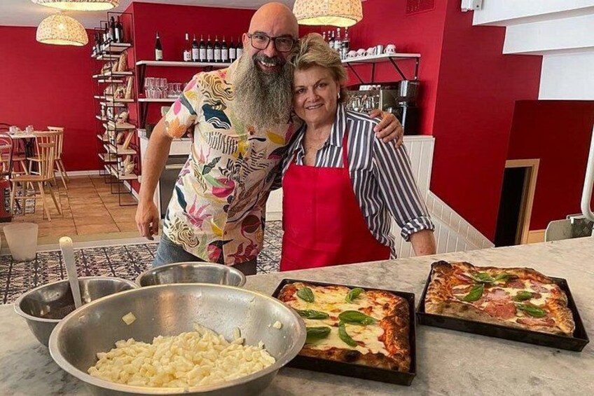 A kitchen with two pizzas on the counter, a bowl of pasta, and a person wearing a red apron. 3