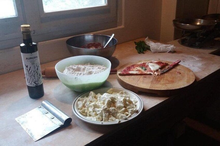A kitchen counter with a bottle of wine, a bowl of flour, a plate of pasta, and a cutting board with a piece of meat. 2