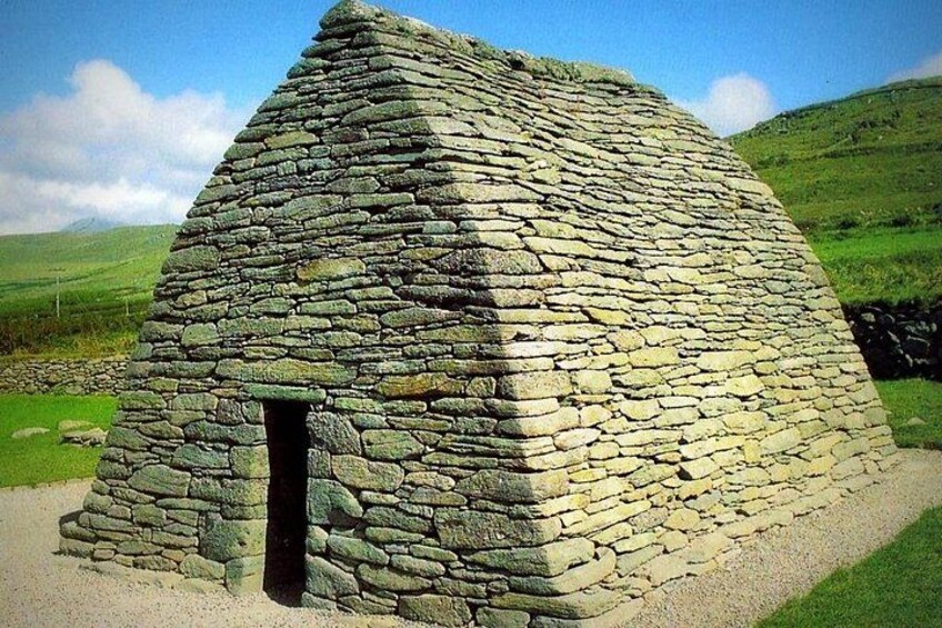 Una estructura de piedra con techo triangular, rodeada por un paisaje cubierto de hierba. 3