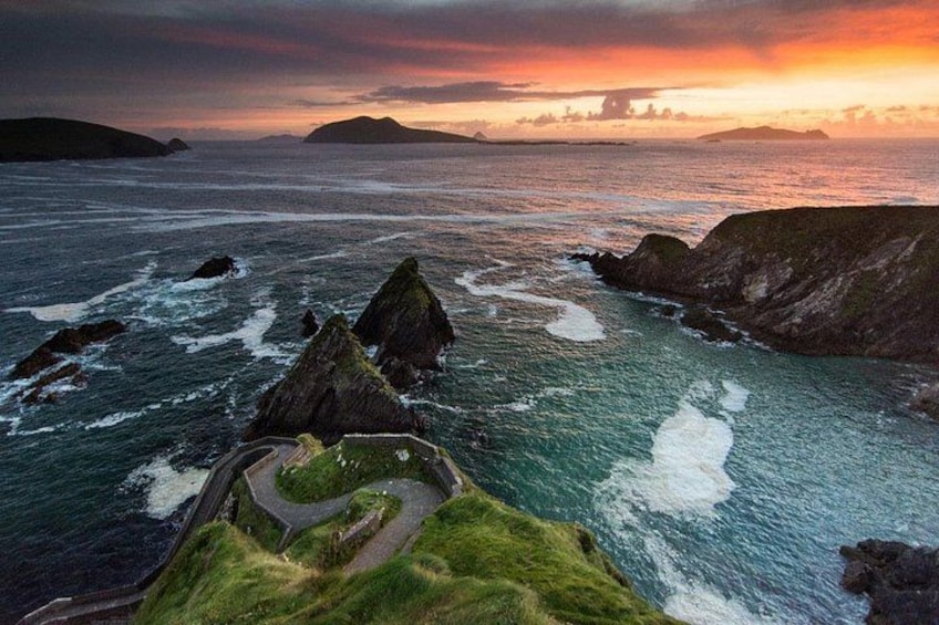 A coastal landscape with rocky outcrops, a winding path, and a sunset over the ocean. 3