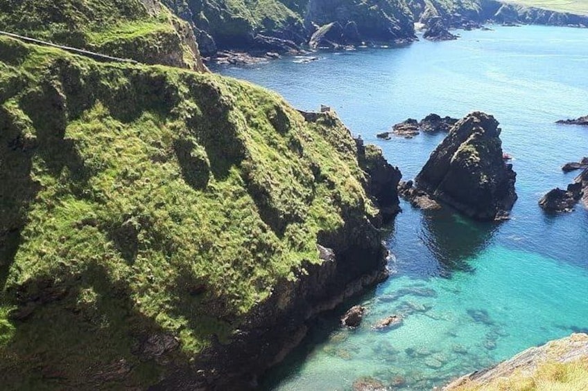 A coastal landscape with green hills, clear blue water, and rocky outcrops. 4