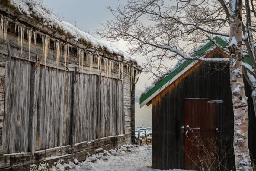 A wooden barn with icicles, a snow-covered roof, and a snow-covered ground. 5