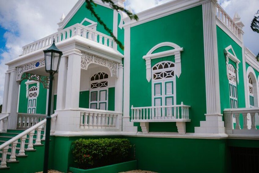 Un edificio verde con detalles blancos, una escalera y ventanas decorativas. 1