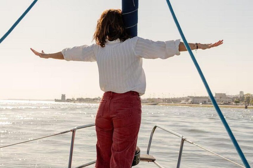 A person standing on a boat with arms outstretched, facing a body of water with a city skyline in the background. 1
