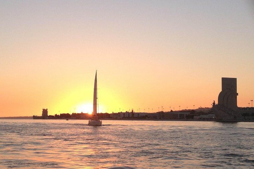 A sunset over a body of water with a sailboat and a large building. 5