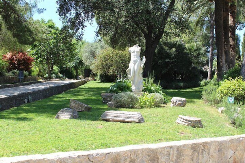 Une statue dans un jardin, avec des bancs en pierre et une végétation luxuriante. 1