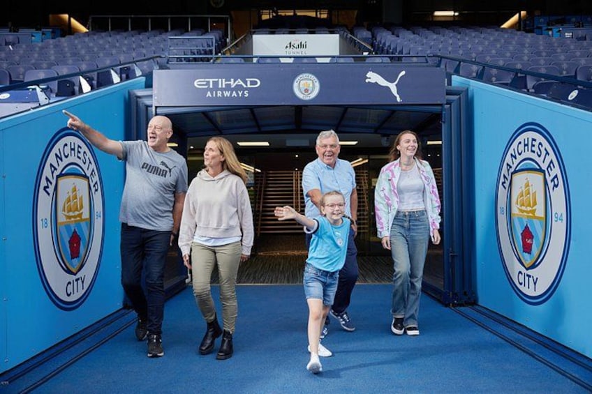 A group of people walking through a tunnel with Manchester City logos and Etihad Airways branding. 3