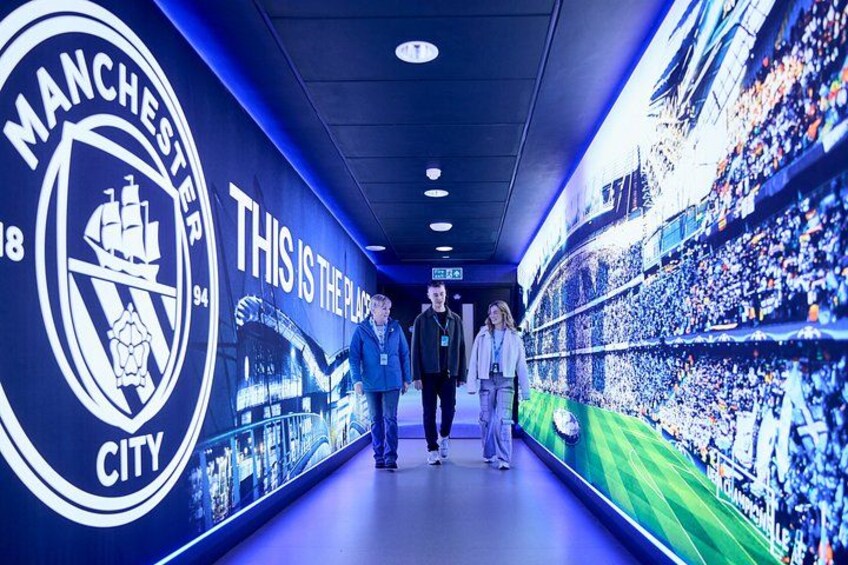 A corridor with a large Manchester City logo and a stadium seating area. 2