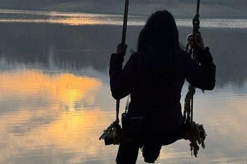 A person on a swing over a calm body of water with reflections. 5