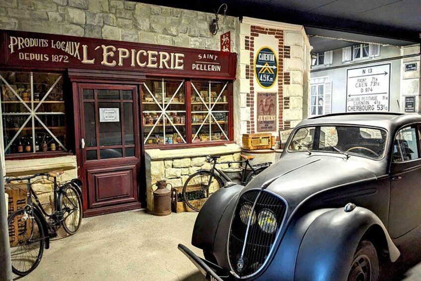 Un coche antiguo estacionado frente a una tienda con un letrero que dice 'L'Epicerie' y bicicletas. 4