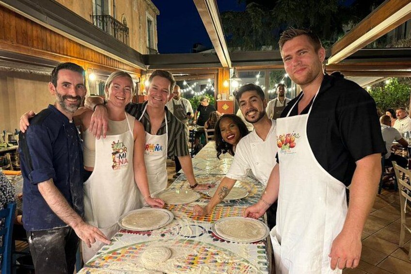 A group of people standing around a table with food items, wearing aprons with logos, in an outdoor dining setting. 2