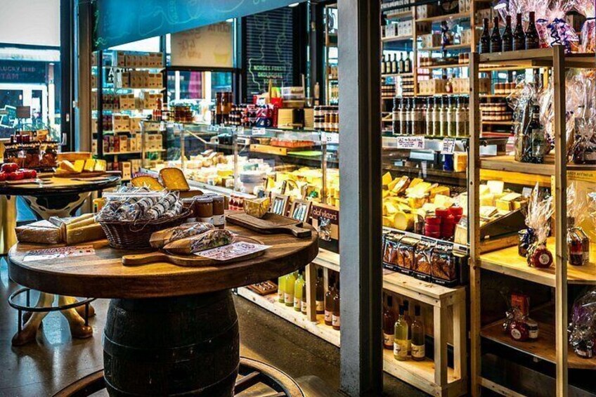 A cheese shop with shelves of various cheeses and a table with cheese samples. 2