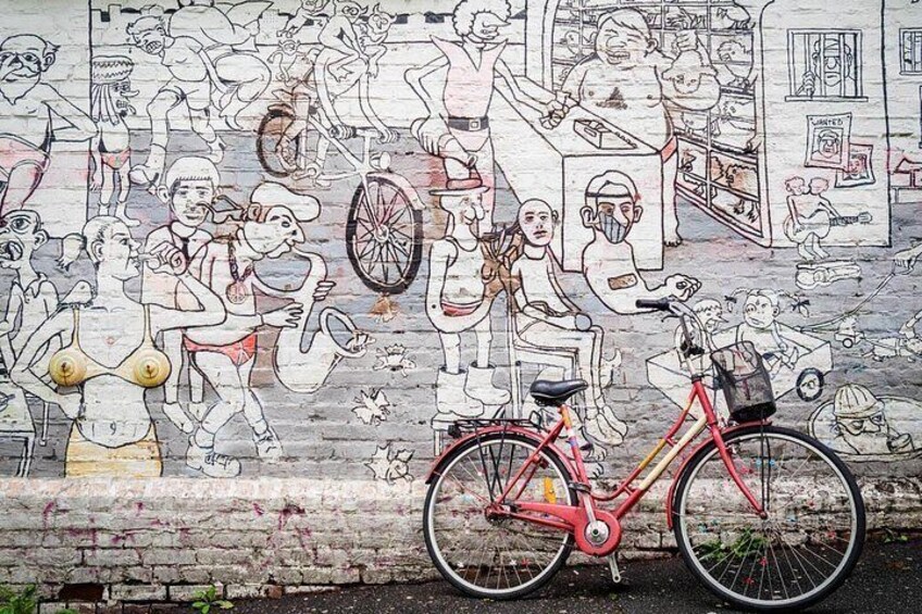 A mural with people and bicycles, a red bicycle in the foreground, and a brick wall. 4