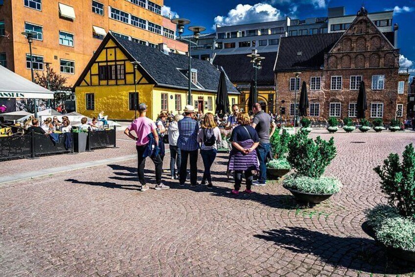 A cobblestone square with people standing and conversing, surrounded by historic buildings with distinct architectural styles. 5