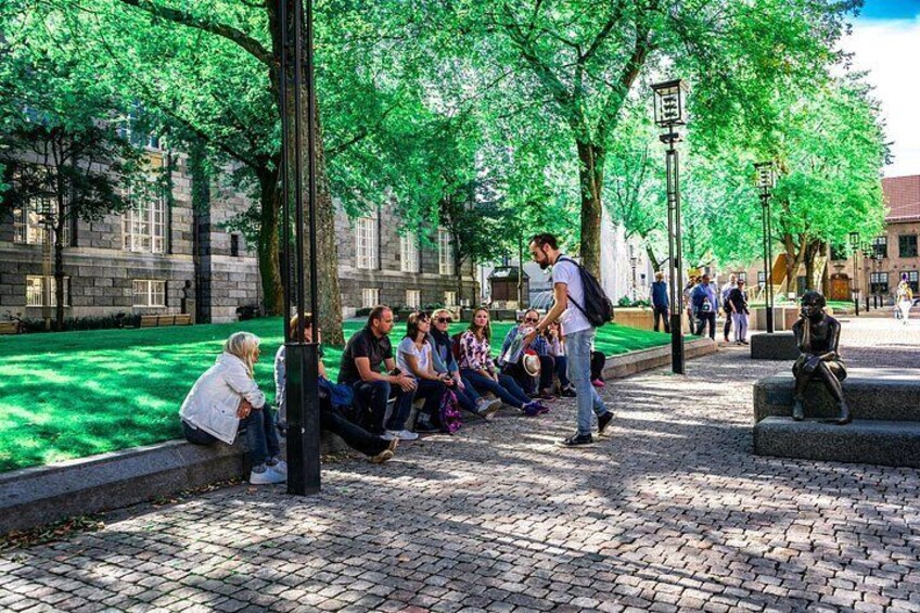 A group of people sitting on a paved area with trees and a building in the background. 3