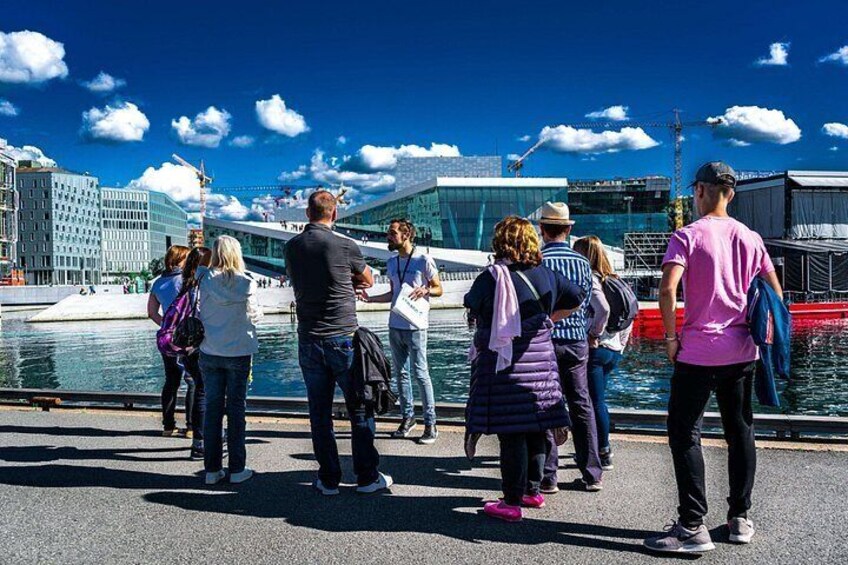 A group of people standing by a waterfront with modern buildings and a clear sky. 2