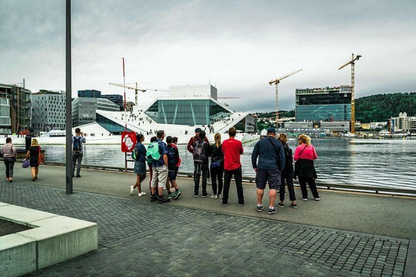 A group of people standing by a waterfront, a modern building, and construction cranes in the background. 2