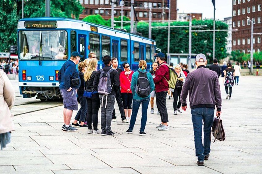 A blue bus with the number 125, people standing on the sidewalk, and buildings in the background. 1