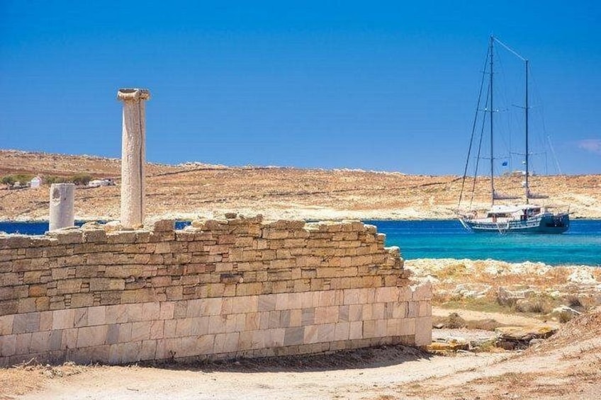 A coastal landscape with a stone wall, a sailboat, and a clear blue sky. 2