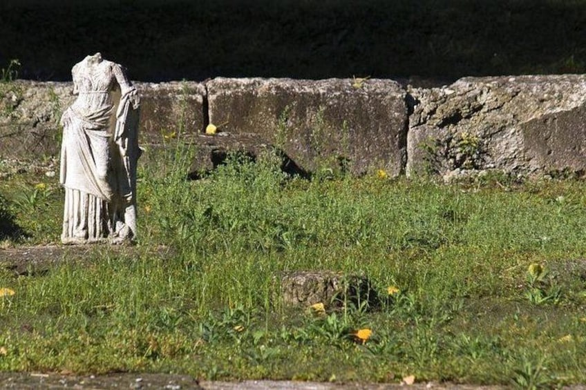 A statue in a grassy field with a stone wall in the background. 2