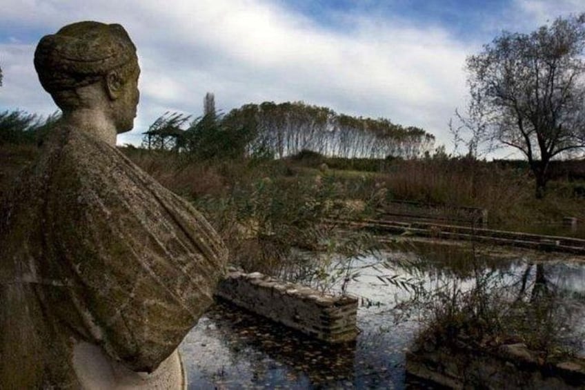 A stone statue overlooking a pond with a bridge and trees in the background. 1