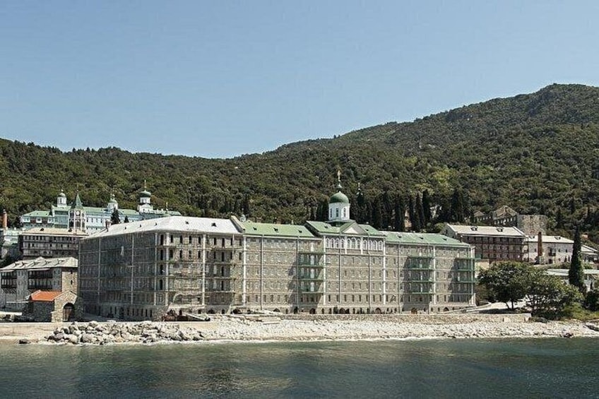 A large building with a green roof and a dome, situated by a body of water with a forested hill in the background. 3