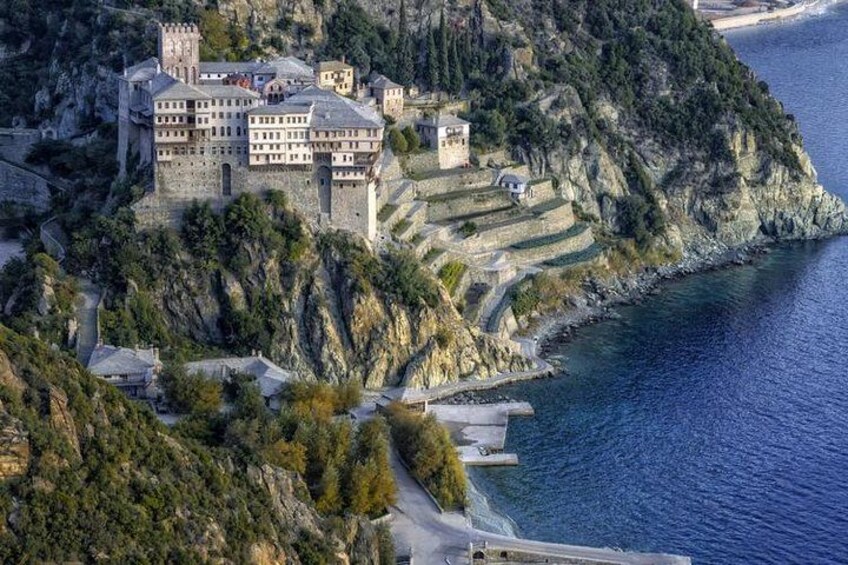 A coastal castle complex with terraced structures, a prominent tower, and a surrounding mountainous landscape. 2