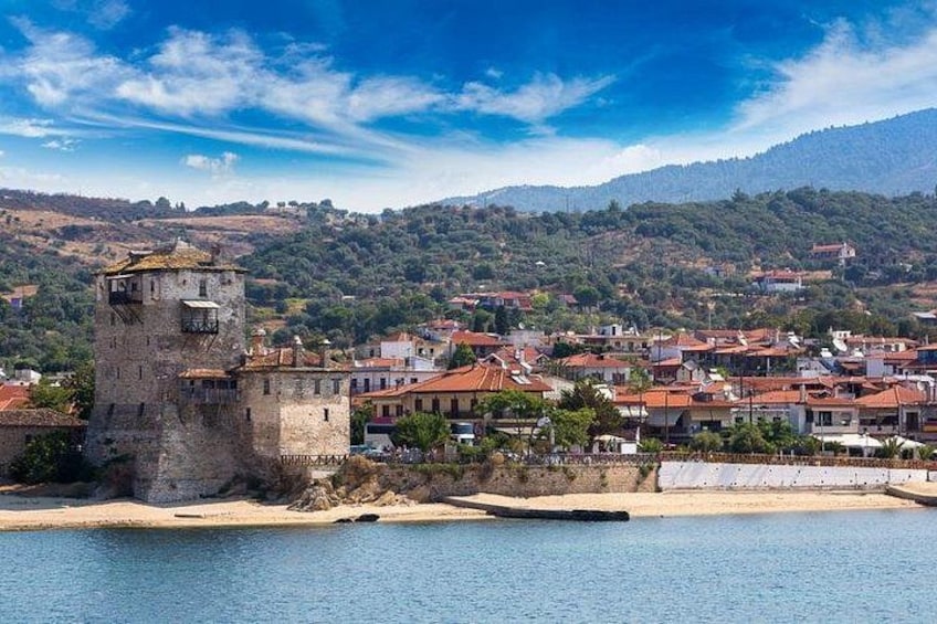 A coastal town with a prominent tower, red-roofed buildings, and a hilly backdrop. 2