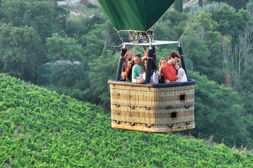 Un globo aerostático de mimbre con pasajeros, sobrevolando un paisaje verde y exuberante. 3