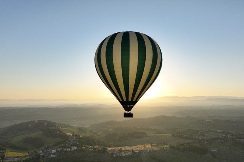 Un globo aerostático vuela sobre un paisaje con colinas y un pueblo. 5