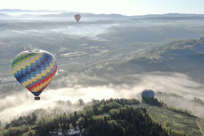 Un globo aerostático sobre un paisaje montañoso con niebla y otro globo a lo lejos. 4