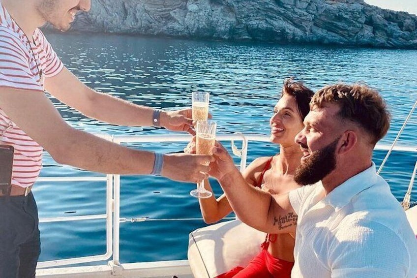 Una persona brindando con una bebida en un barco, otra persona sosteniendo un vaso y un litoral rocoso al fondo. 5